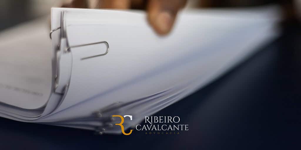 Documentos grampeados perto de uma mão, logo da Ribeiro Cavalcante Advocacia na imagem.