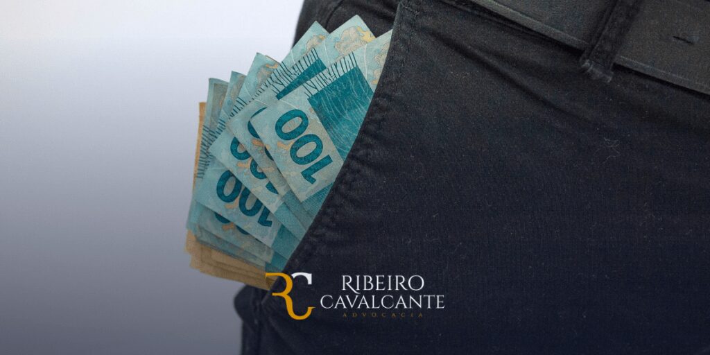 Notas de cem reais saindo do bolso de uma calça preta. Logotipo da escritório de advocacia Ribeiro Cavalcante.