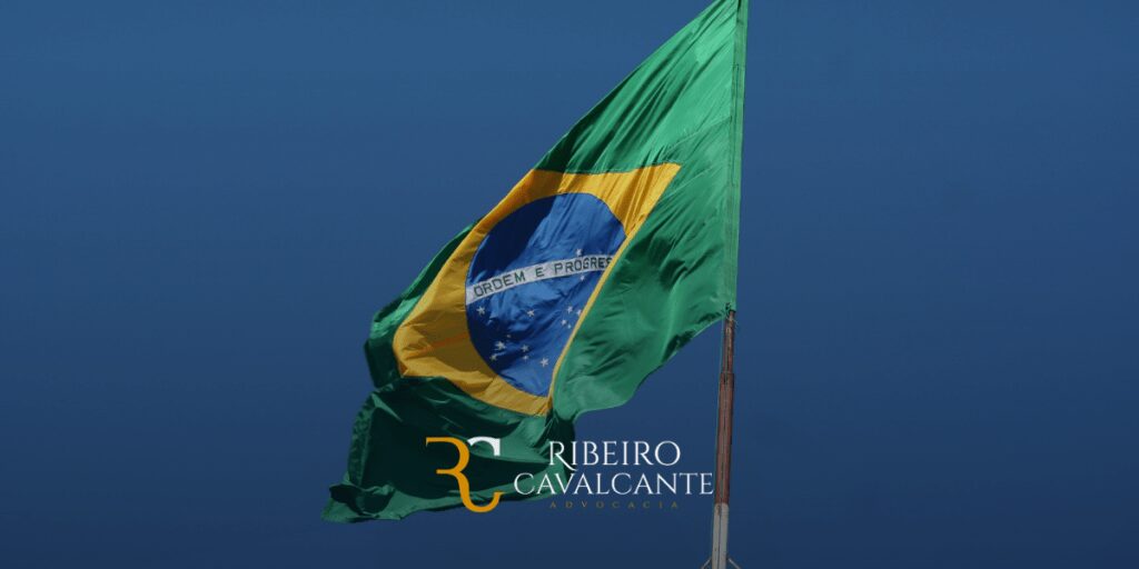 Bandeira do Brasil com logotipo do escritório Ribeiro Cavalcante Advocacia ao fundo de céu azul.