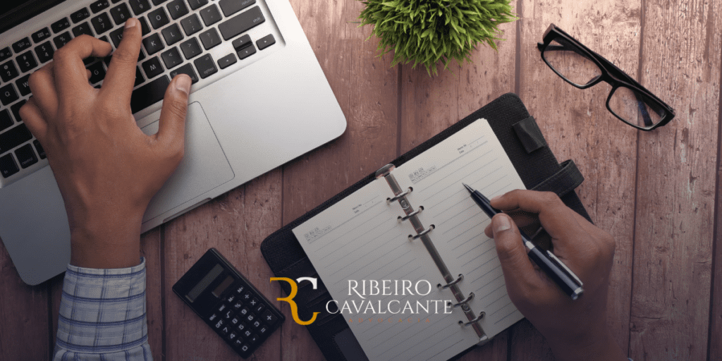 Pessoa trabalhando em um laptop com notas e calculadora sobre a mesa. Ribeiro Cavalcante Advocacia.