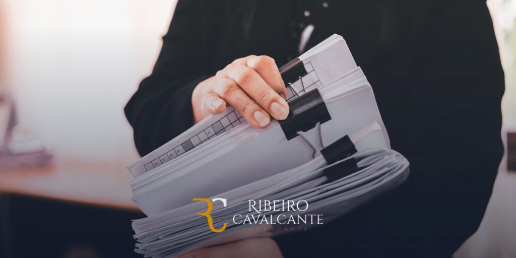 Pessoa segurando arquivos de papel com clipes. Logotipo Ribeiro Cavalcante Advocacia visível na parte inferior.