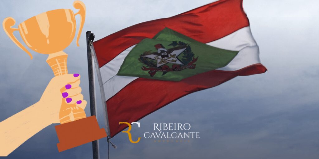 Bandeira de Santa Catarina ao vento com troféu em primeiro plano e logotipo da Ribeiro Cavalcante Advocacia.