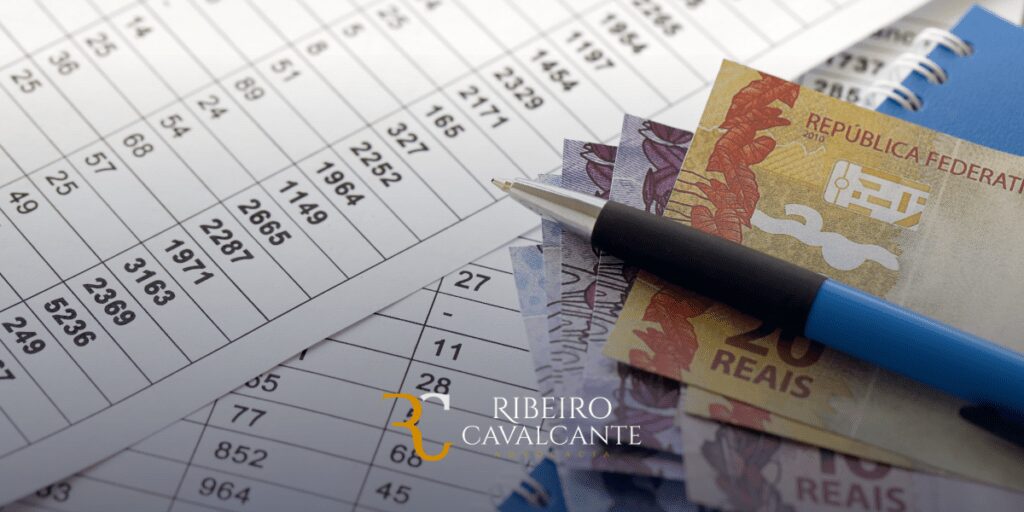 Dinheiro brasileiro e tabela financeira com caneta, representando cálculos e planejamento financeiro. Logo Ribeiro Cavalcante.