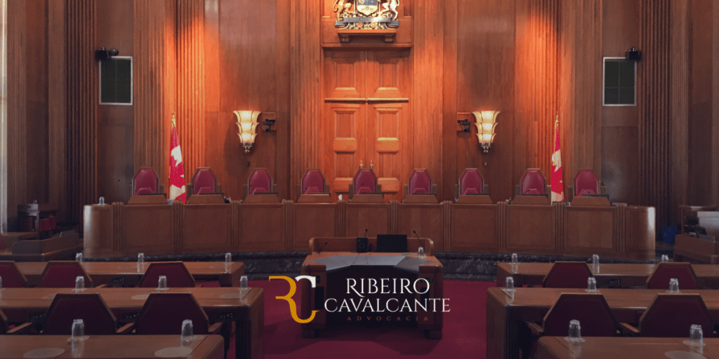 Sala de tribunal com cadeiras de couro vermelho, bandeira e brasão. Logo da Ribeiro Cavalcante Advocacia em destaque.