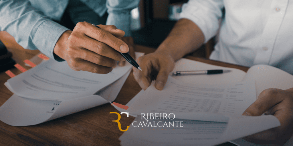 Advogados analisando documentos jurídicos no escritório Ribeiro Cavalcante Advocacia. Logotipo da empresa visível na imagem.