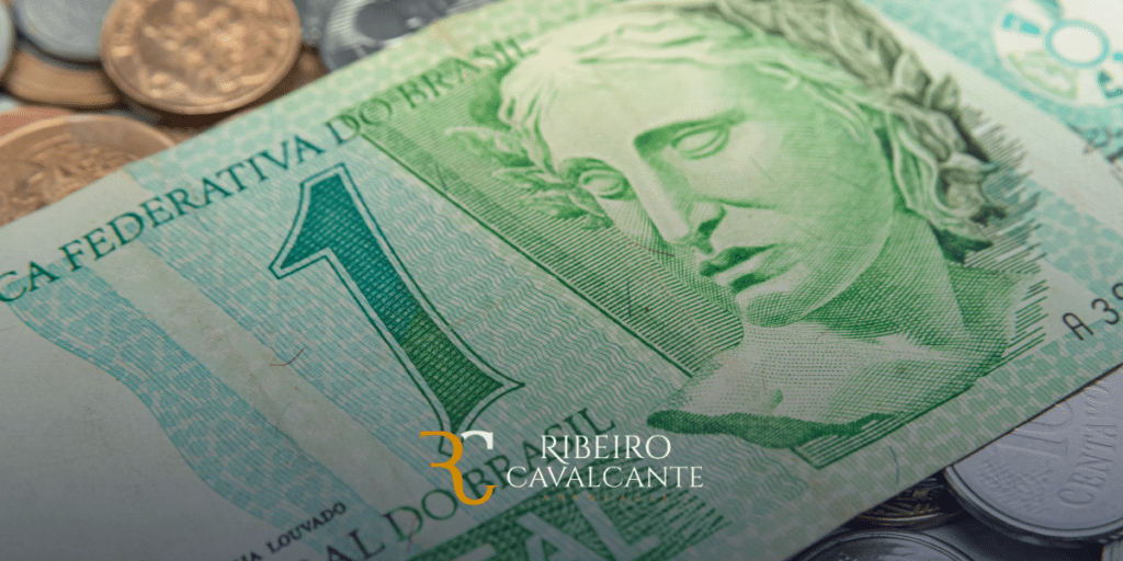Nota de um real e moedas brasileiras, com logotipo Ribeiro Cavalcante Advocacia em destaque.