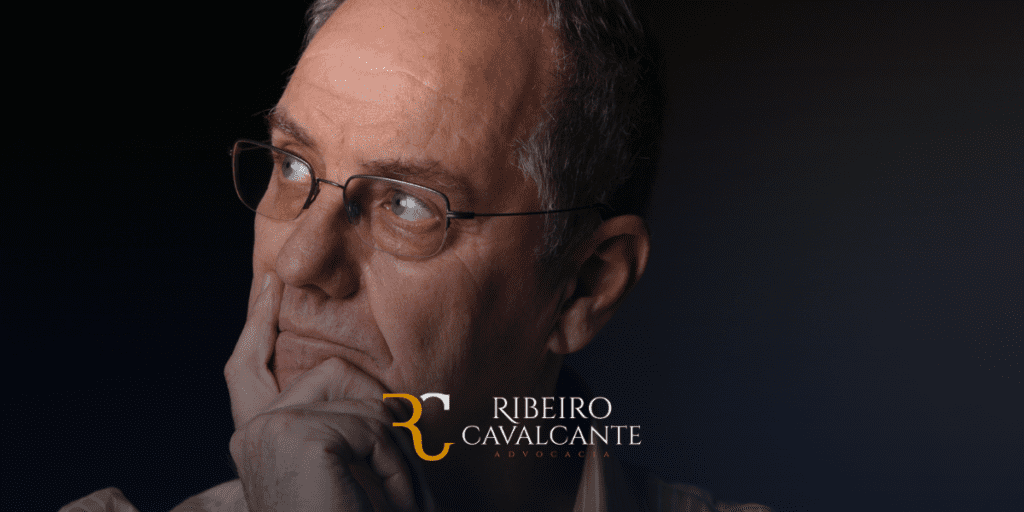 Homem pensativo com óculos, logotipo Ribeiro Cavalcante Advocacia ao fundo. Fundo escuro.