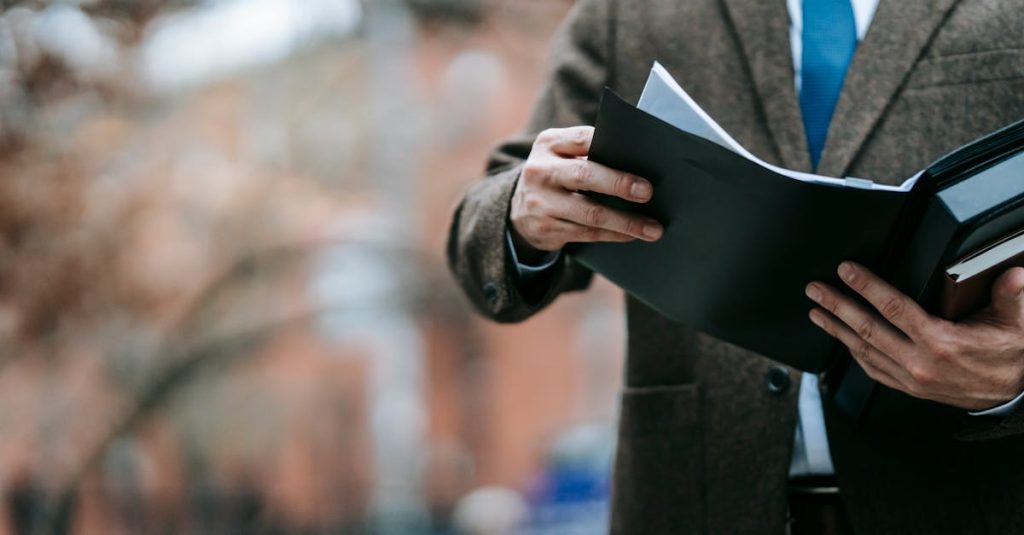 Homem de terno e gravata segurando e analisando uma pasta com documentos em ambiente externo. — Foto: Vanessa Garcia