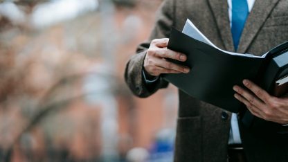 Homem de terno e gravata segurando e analisando uma pasta com documentos em ambiente externo. — Foto: Vanessa Garcia