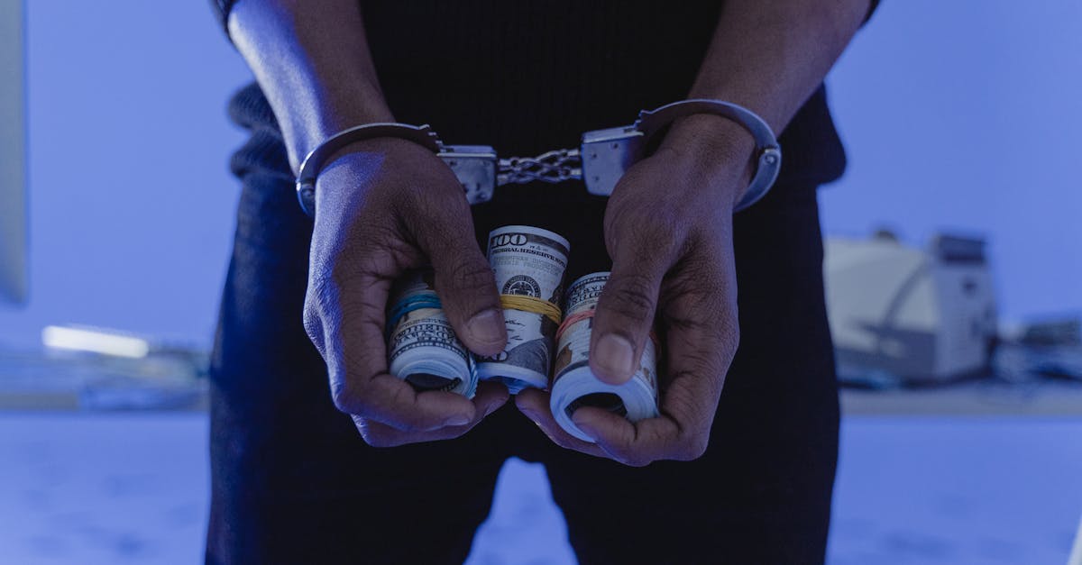 Close das mãos de uma pessoa algemada segurando rolos de notas de dólar em um ambiente com iluminação azulada. — Foto: Tima Miroshnichenko