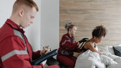 Socorristas em uniformes vermelhos atendendo uma paciente em casa e anotando informações em uma prancheta. — Foto: Pavel Danilyuk