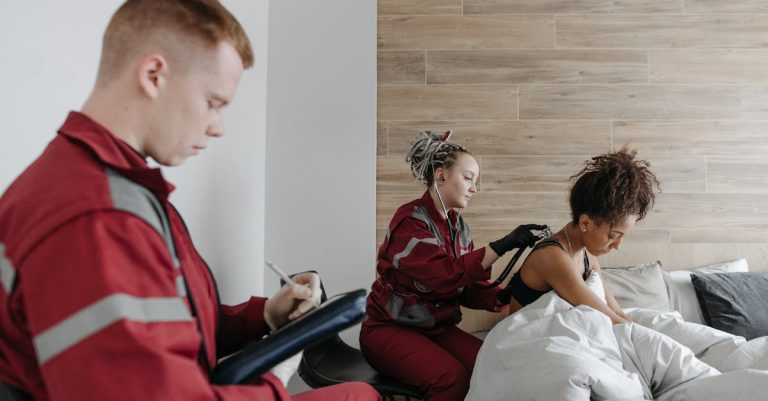 Socorristas em uniformes vermelhos atendendo uma paciente em casa e anotando informações em uma prancheta. — Foto: Pavel Danilyuk