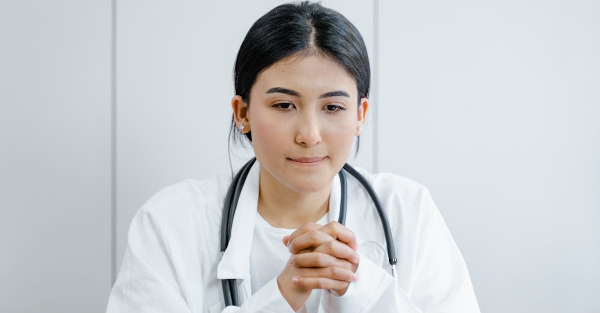 Médica com jaleco branco e estetoscópio no pescoço com as mãos entrelaçadas em um ambiente profissional. — Foto: Tima Miroshnichenko