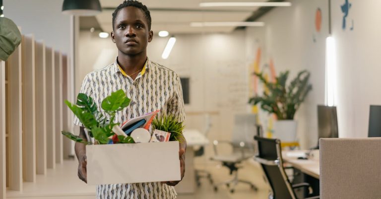 Homem negro segurando caixa com pertences pessoais em um escritório, representando demissão ou saída do emprego. — Foto: Mikhail Nilov