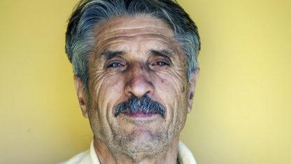Retrato de um homem idoso com bigode e cabelos grisalhos olhando para a câmera em fundo amarelo. — Foto: Pexels