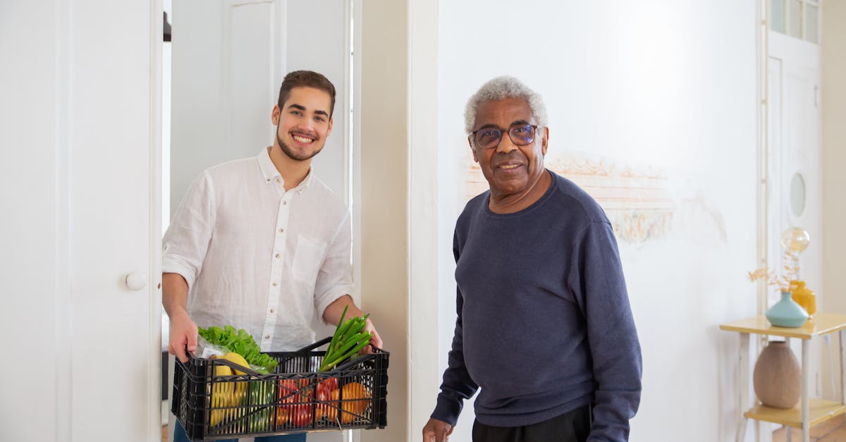 Homem jovem entregando cesta de alimentos para um senhor idoso sorridente em uma residência. — Foto: Kampus Production