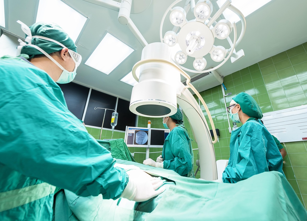 Equipe médica com trajes cirúrgicos verdes realizando procedimento em centro cirúrgico moderno com equipamentos. — foto: sasint
