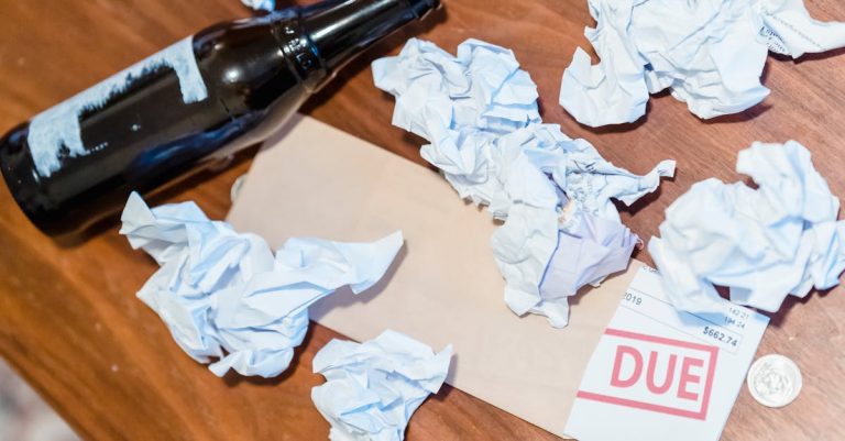 Papéis amassados, uma garrafa vazia e uma fatura com o carimbo 'DUE' sobre uma mesa de madeira. — Foto: Nicola Barts