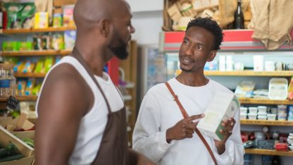 Homem em um mercado apontando para a embalagem de um produto enquanto conversa com o atendente. — Foto: Kampus Production