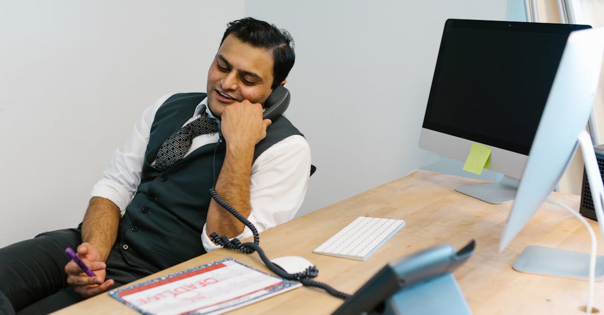 Homem de colete e gravata sorrindo ao telefone em uma mesa de escritório com computador e documentos. — Foto: RDNE Stock project