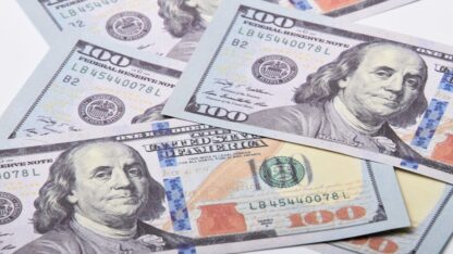 Diversas notas de cem dólares americanos espalhadas sobre uma superfície branca. — Foto: adrian vieriu