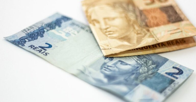 Cédulas de dois e cinquenta reais brasileiros sobre uma superfície branca em ângulo aproximado. — Foto: Daniel Dan