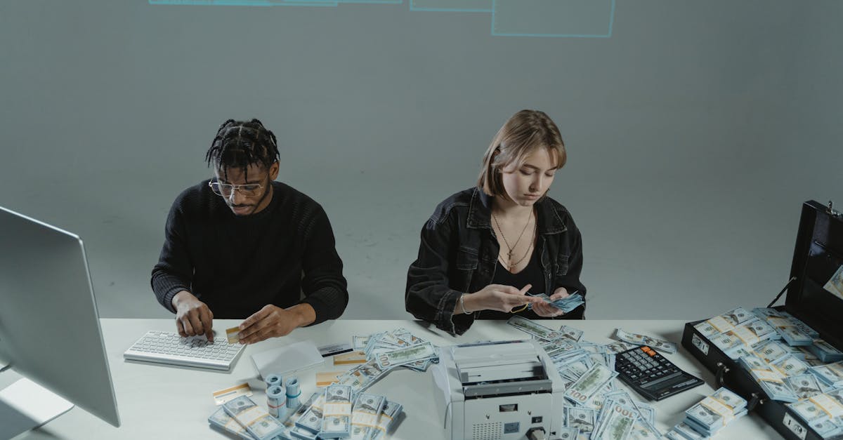 Duas pessoas sentadas à mesa contando grandes pilhas de notas de dólar com auxílio de uma máquina de contar dinheiro. — Foto: Tima Miroshnichenko