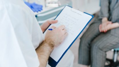 Médico de jaleco branco escrevendo em uma prancheta durante consulta com paciente em consultório. — Foto: SHVETS production