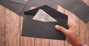 Mão segurando um envelope preto aberto com notas de dinheiro dentro sobre uma mesa de madeira. — Foto: Towfiqu barbhuiya