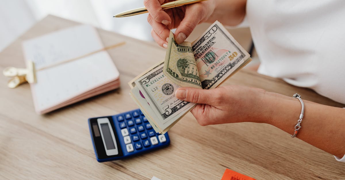 Pessoa contando notas de dinheiro sobre uma mesa com calculadora e caderno, representando planejamento financeiro. — Foto: www.kaboompics.com