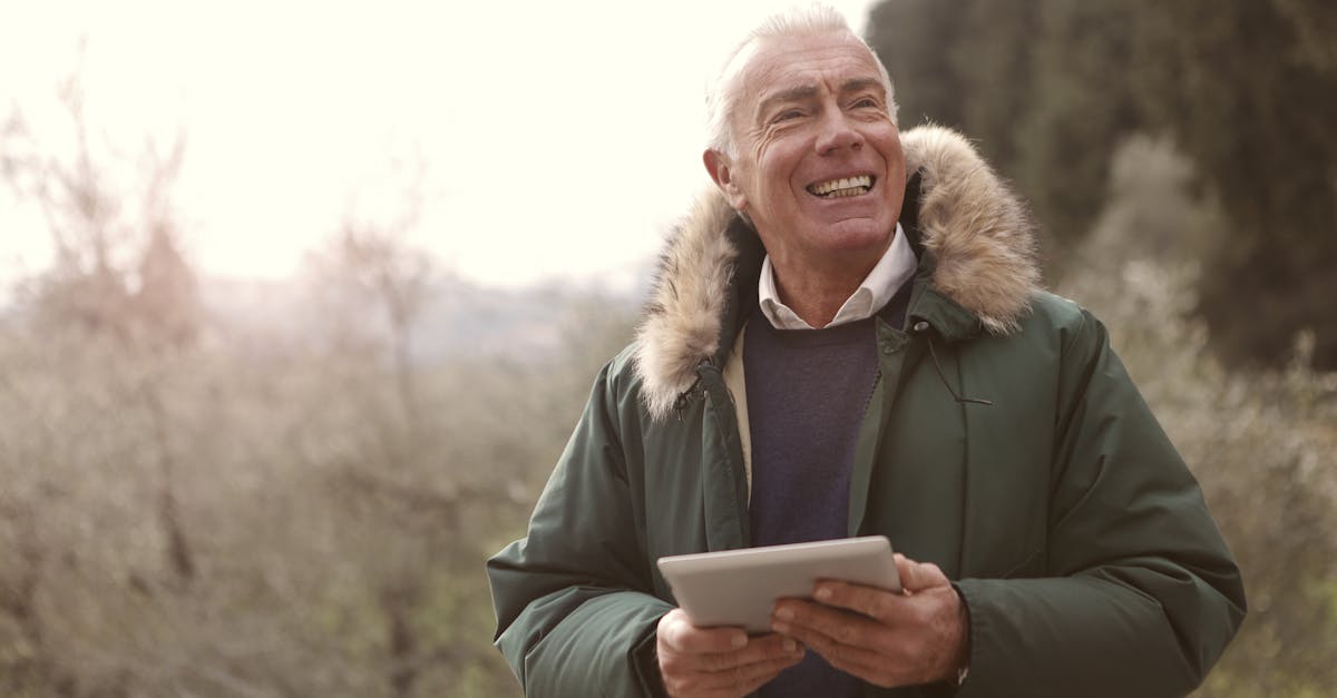 Homem idoso sorridente usando um tablet ao ar livre vestindo casaco de inverno. — Foto: Andrea Piacquadio