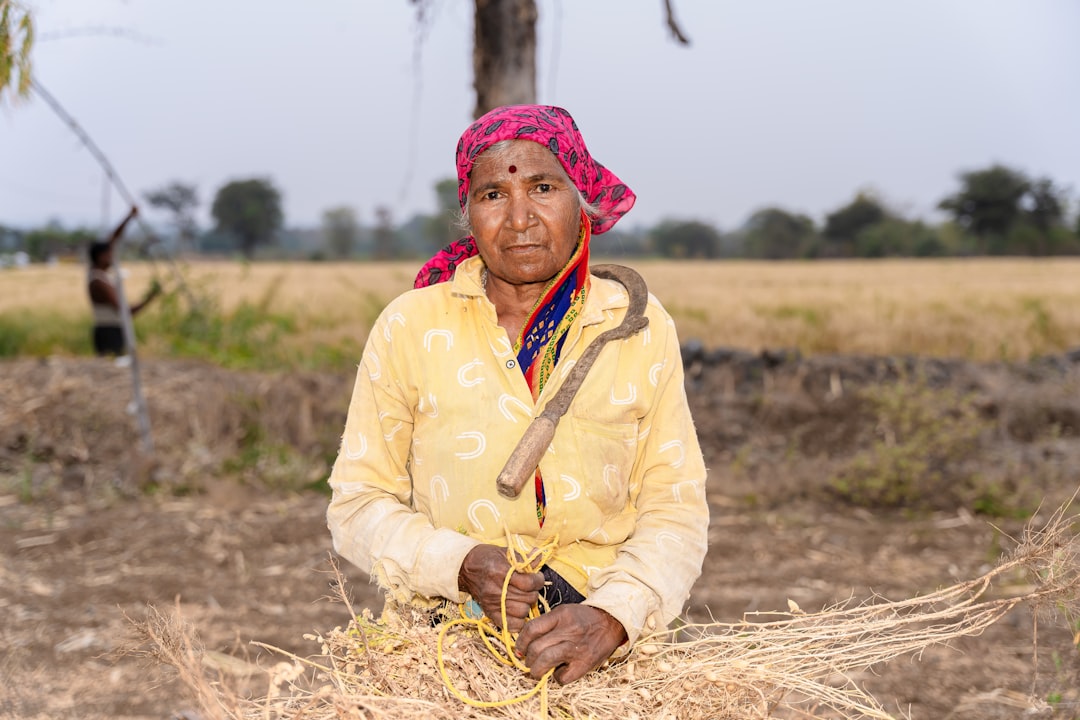 Mulher idosa trabalhando no campo com uma foice sobre o ombro em uma área rural. — Foto: EqualStock
