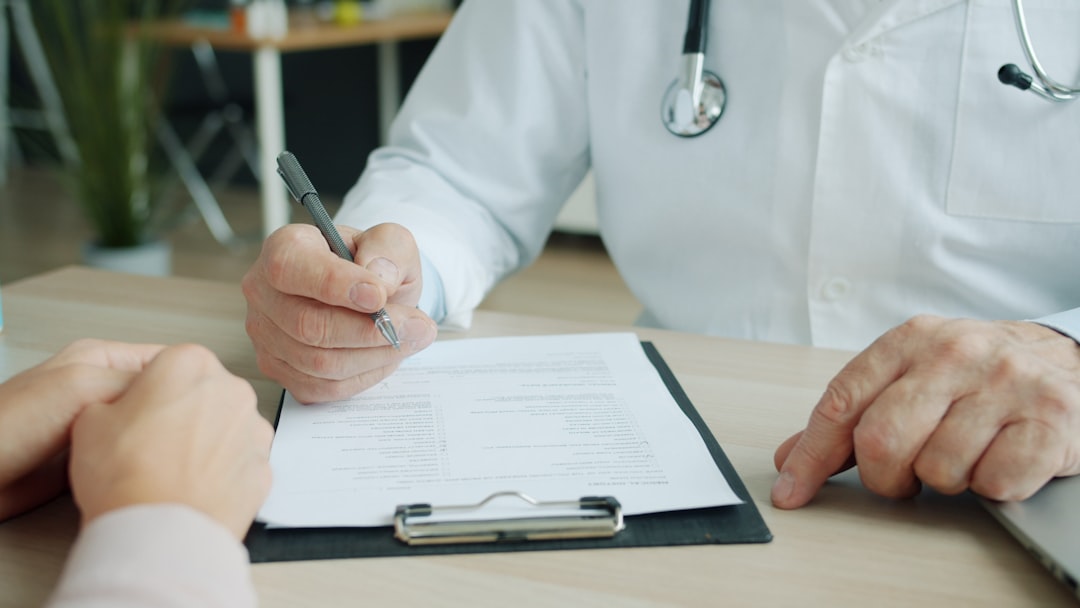 Médico de jaleco branco com estetoscópio escrevendo em formulário médico durante consulta com paciente. — Foto: Vitaly Gariev