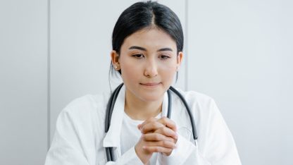 Médica com estetoscópio no pescoço e mãos entrelaçadas em um ambiente profissional de saúde. — Foto: Tima Miroshnichenko