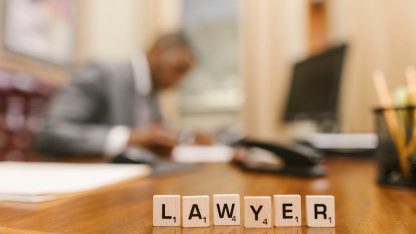 Blocos de madeira formando a palavra Lawyer sobre mesa de escritório com advogado desfocado ao fundo. — Foto: RDNE Stock project