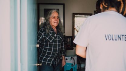Pessoa voluntária conversando com um senhor idoso na porta de uma residência. — Foto: RDNE Stock project