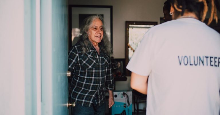 Pessoa voluntária conversando com um senhor idoso na porta de uma residência. — Foto: RDNE Stock project