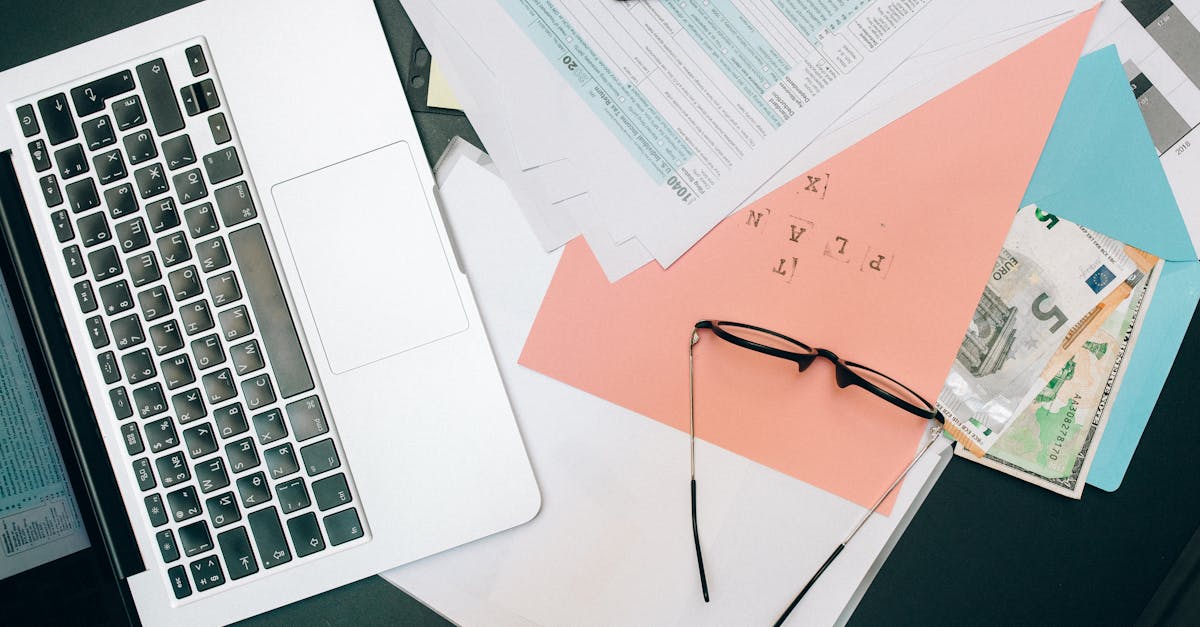 Vista superior de um notebook, óculos, documentos de papel e notas de dinheiro sobre uma mesa de trabalho. — Foto: Nataliya Vaitkevich