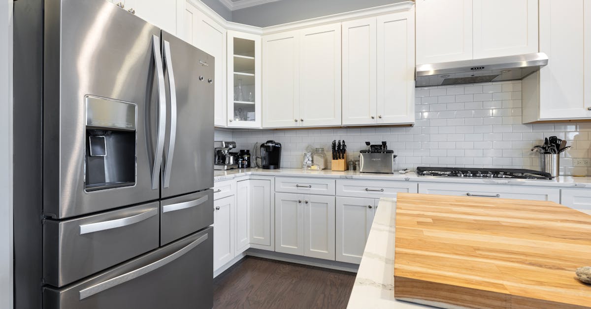 Cozinha moderna com geladeira de aço inoxidável em destaque e armários brancos ao fundo. — Foto: Curtis Adams