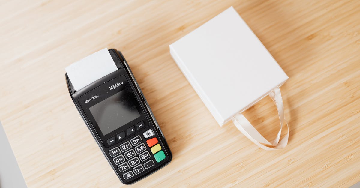 Vista superior de uma máquina de cartão de crédito e uma sacola de compras branca sobre uma mesa de madeira. — Foto: www.kaboompics.com