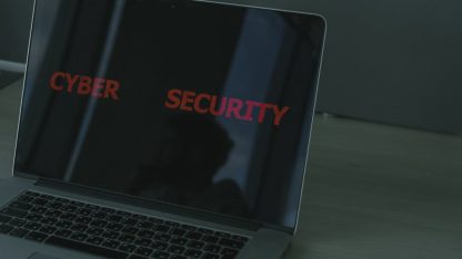 Notebook aberto exibindo as palavras Cyber Security em letras vermelhas na tela escura. — Foto: cottonbro studio