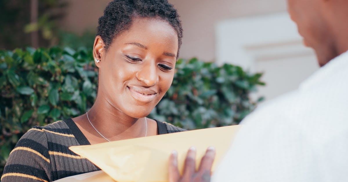 Mulher sorridente recebendo ou entregando um envelope pardo e uma caixa de papelão para outra pessoa. — Foto: Kindel Media