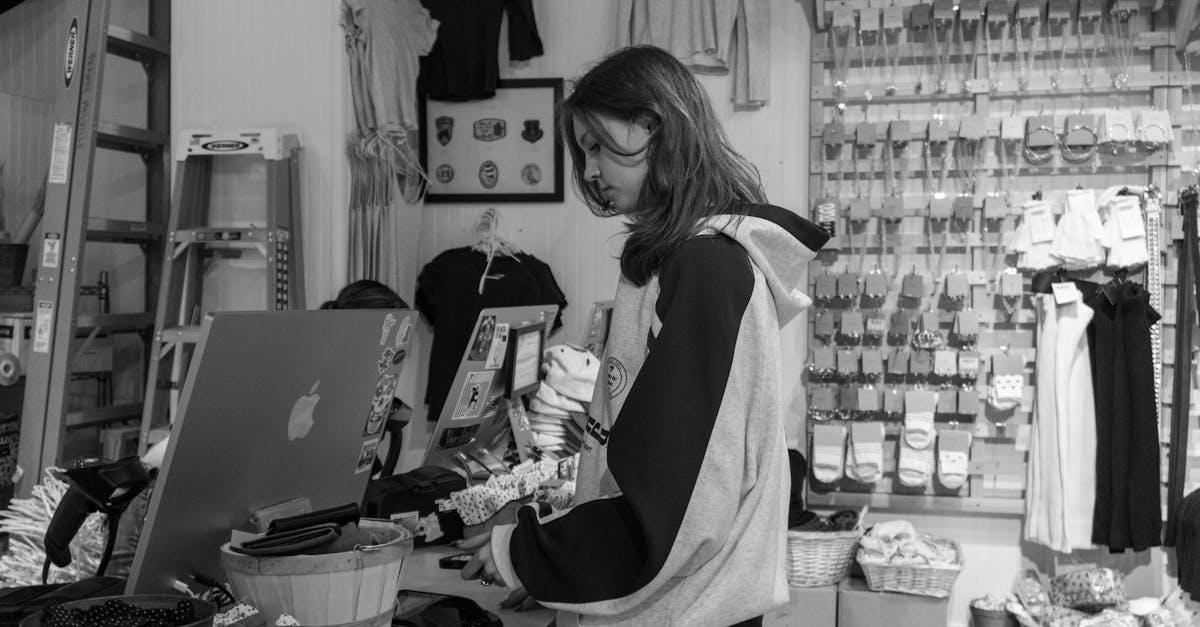 Mulher em frente ao balcão de uma loja de roupas com computador e prateleiras ao fundo em preto e branco. — Foto: Naveen Ketterer