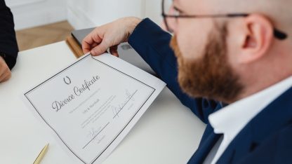 Advogado de terno segurando um documento oficial com o título Divorce Certificate sobre uma mesa branca. — Foto: www.kaboompics.com