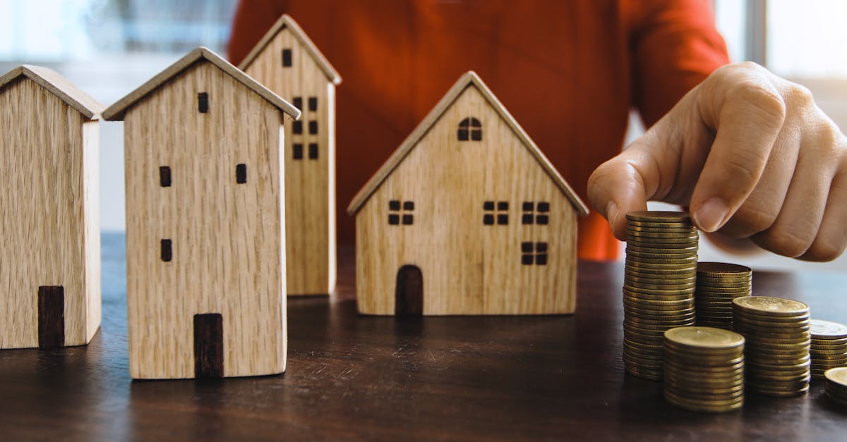 Mão organizando pilhas de moedas ao lado de pequenas casas de madeira sobre uma mesa. — Foto: Khwanchai Phanthong