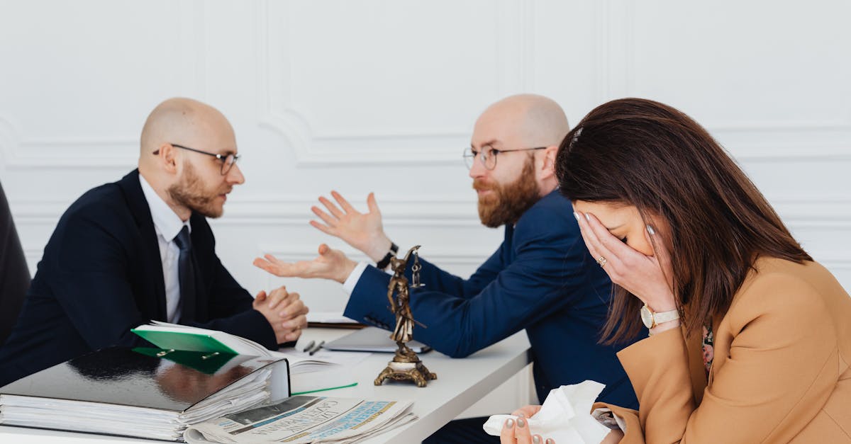 Dois advogados em reunião com uma mulher emocionada em um escritório com a estátua da justiça sobre a mesa. — Foto: www.kaboompics.com