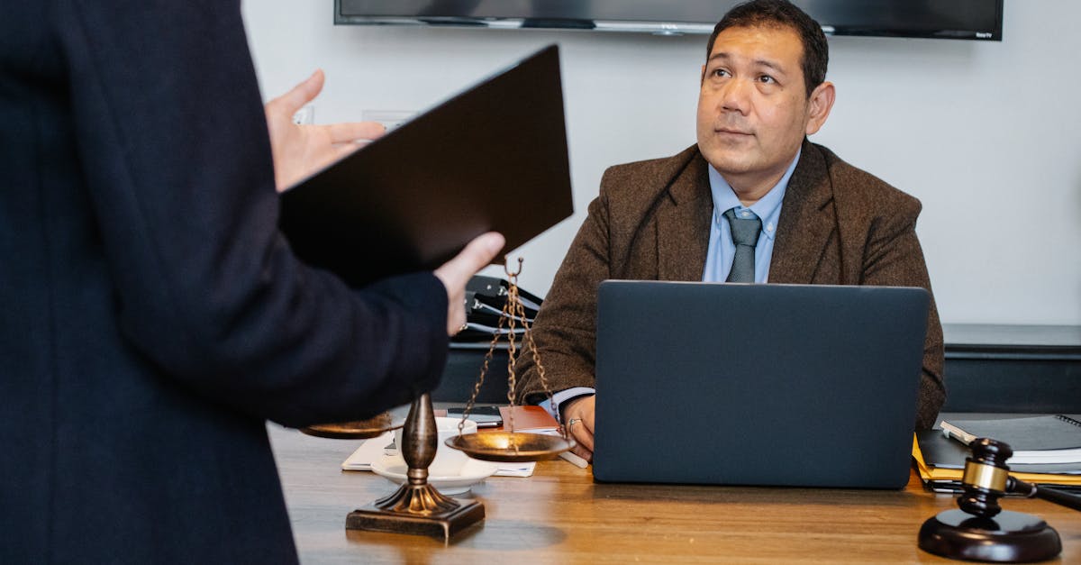 Advogado em escritório com notebook, balança da justiça e martelo, conversando com colega que segura uma pasta. — Foto: Sora Shimazaki