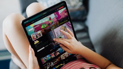 Criança sentada no sofá usando um tablet para assistir a desenhos animados em um aplicativo de streaming. — Foto: www.kaboompics.com