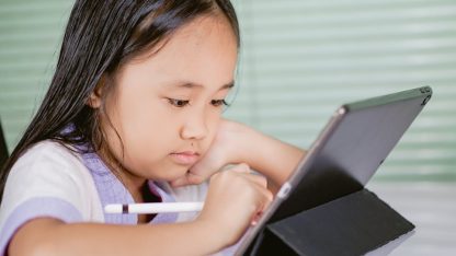 Menina concentrada utilizando um tablet com caneta digital em uma mesa. — Foto: Ryan Delfin