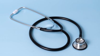 Um estetoscópio médico preto e prata repousando sobre uma superfície azul clara uniforme. — Foto: Etatics Inc.